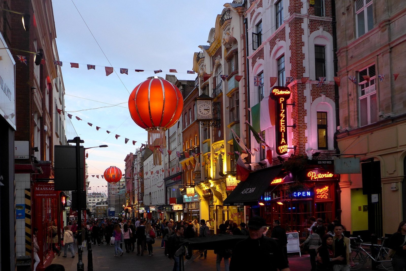 Wardour Street in Soho at dusk, with neon signs and lanterns above the crowds