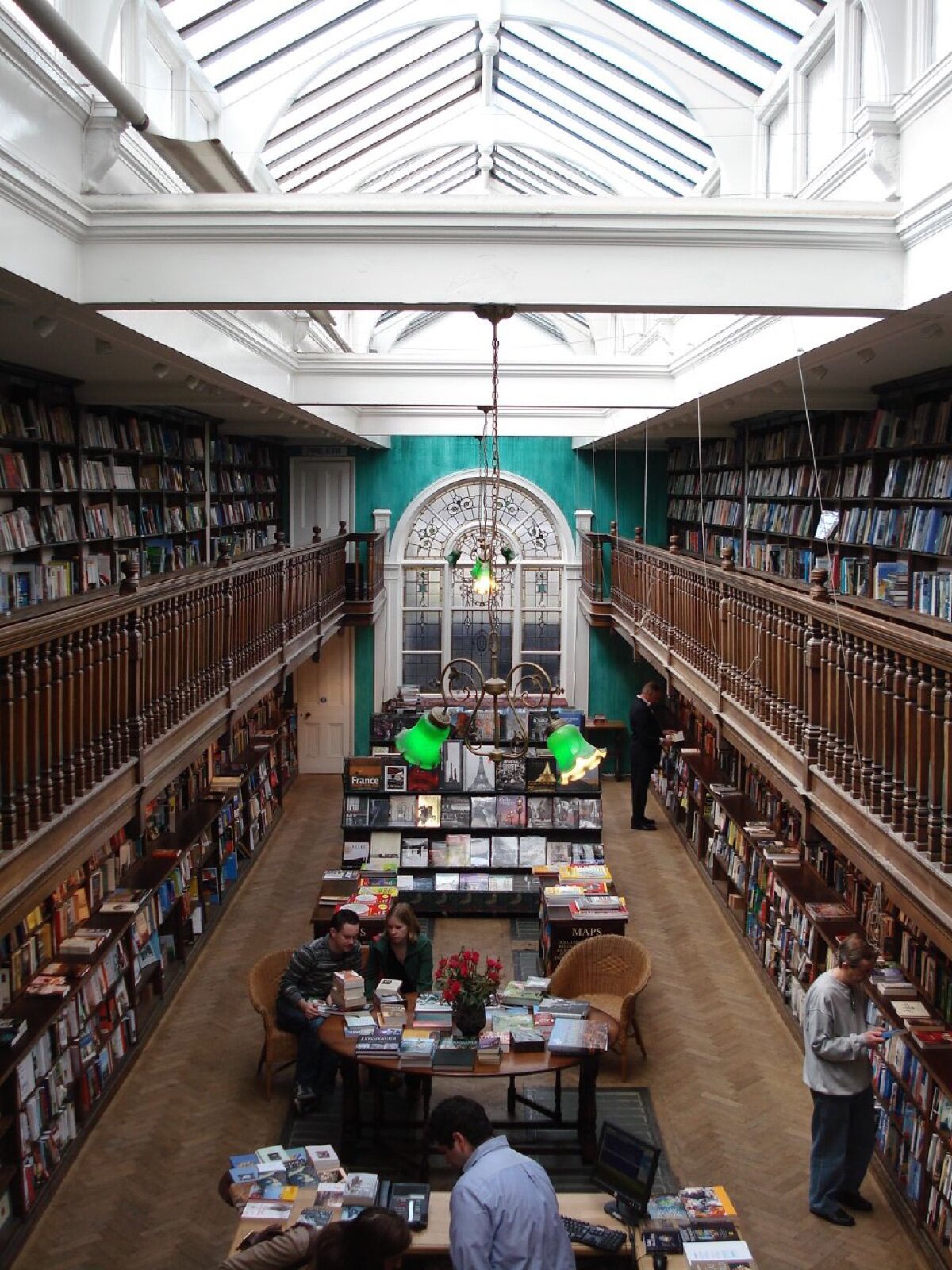 The long oak gallery of Daunt Books in Marylebone, lit by a skylight and a stained glass window