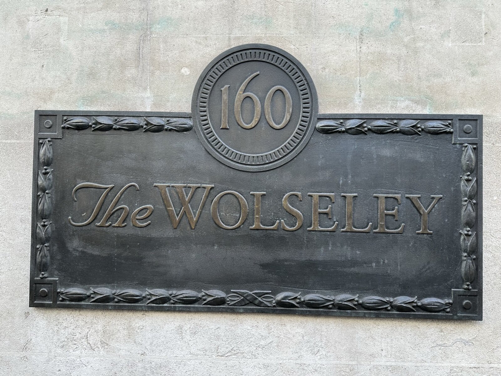 A bronze plaque reading 160 The Wolseley on the stone wall outside the restaurant on Piccadilly