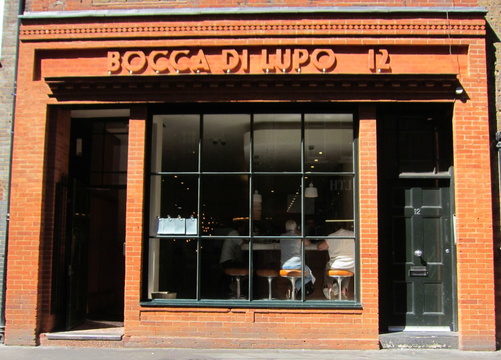 The red-brick frontage of Bocca di Lupo on Archer Street in Soho, with its name in raised letters above a large window and diners at the counter inside
