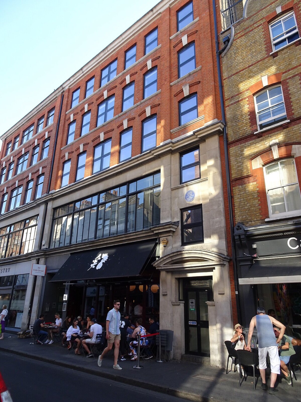 The red-brick building at 54 Frith Street in Soho, with people sitting at tables outside at street level