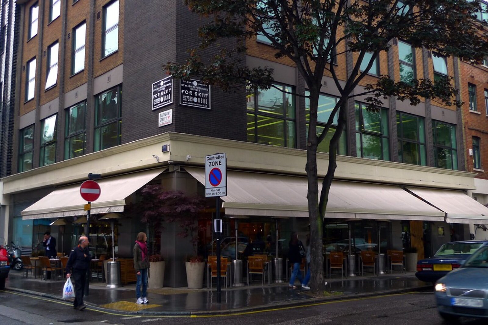 The corner site of Roka and the Shochu Lounge on Charlotte Street in Fitzrovia, with awnings over pavement tables on a wet day