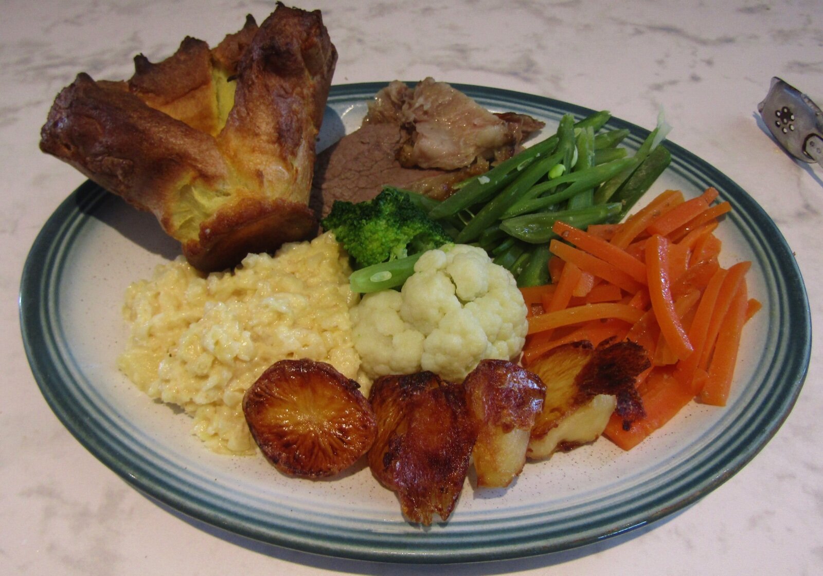 A plate of roast beef with a Yorkshire pudding, roast potatoes, cauliflower cheese, carrots and greens