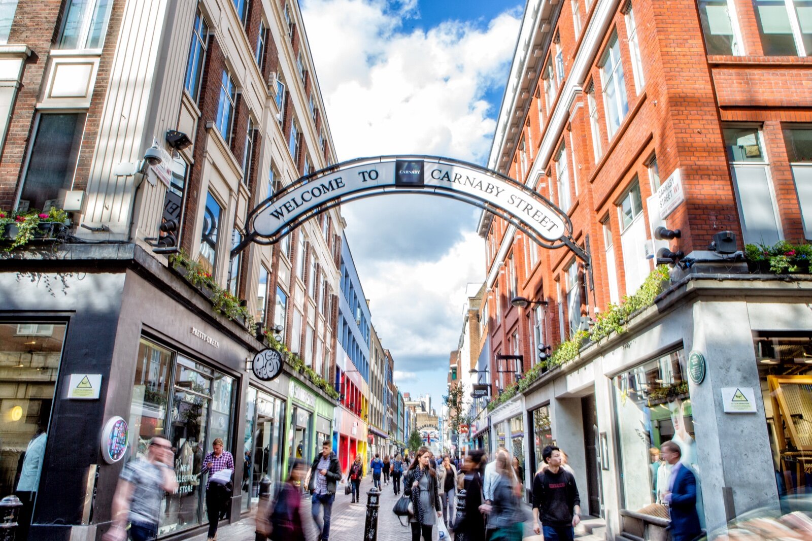 The Welcome to Carnaby Street arch over the pedestrianised street, with red brick buildings and shoppers below
