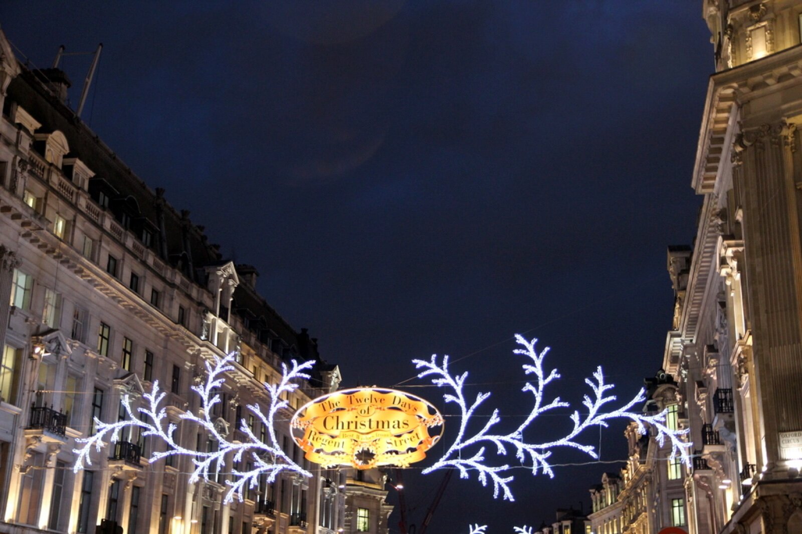 Illuminated Christmas decorations strung across Regent Street at night between the curved stone facades