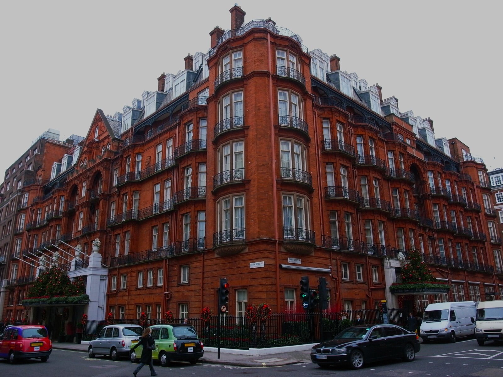 The red brick corner of Claridge's hotel at Brook Street and Davies Street in Mayfair, dressed with Christmas garlands, with black cabs at the kerb