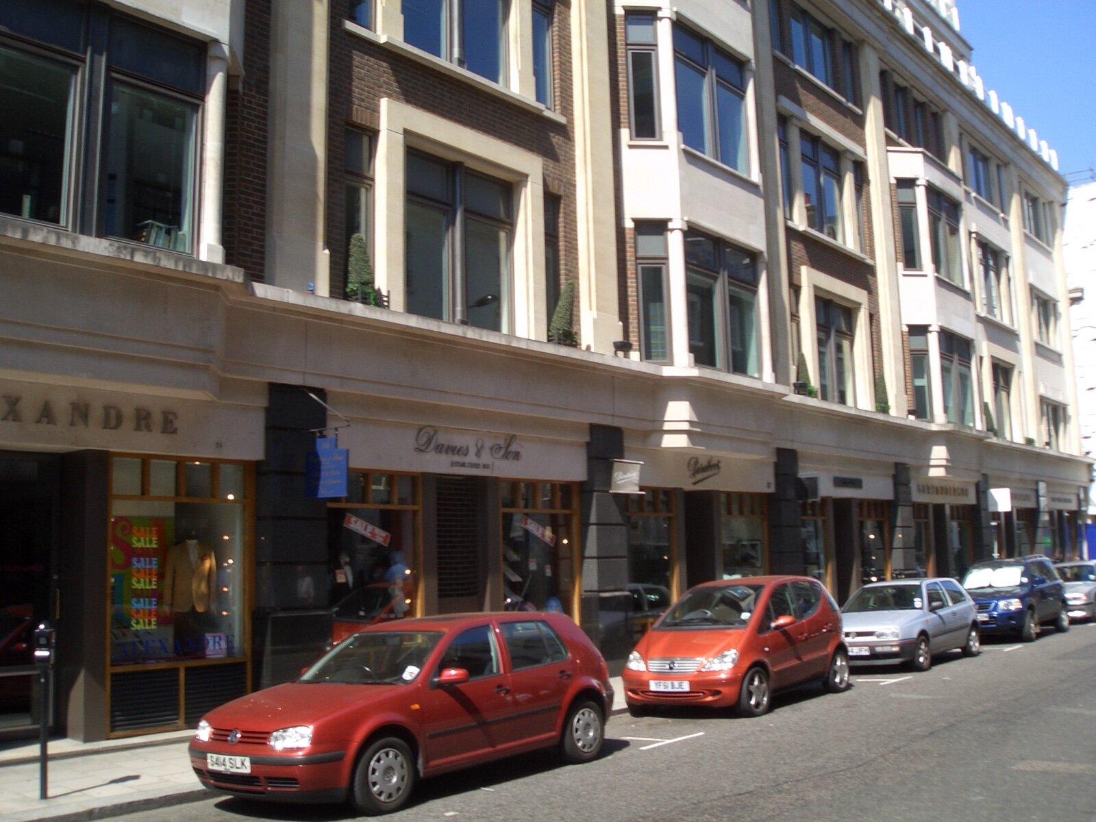 A row of tailors' shopfronts on Savile Row, including Davies and Son, with cars parked outside