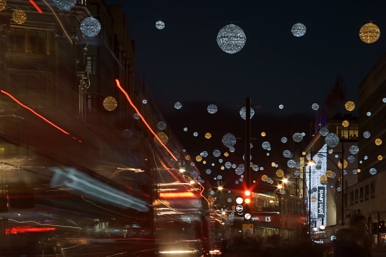 Oxford Street at night in 2015 with silver and gold globe Christmas lights hanging over the road, a red bus and a John Lewis sign